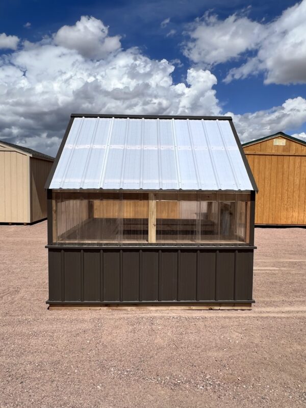 The 8x8 Greenhouse shown from the side against a backdrop of the bright blue sky and fluffy white clouds, with several other sheds in the background.