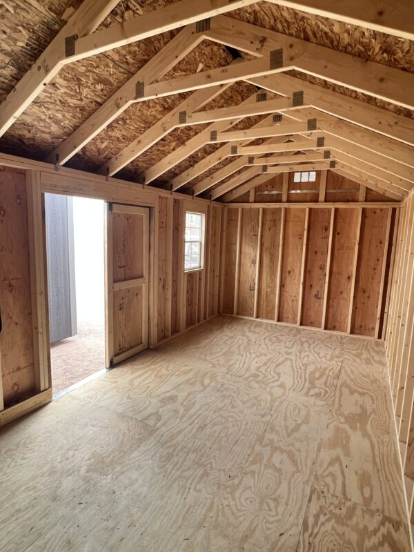 Within the 10x20 Gable Style storage shed, a beam of light casts a radiant glow upon the hardwood planks and lumber adorning the ceiling, walls, and floor.