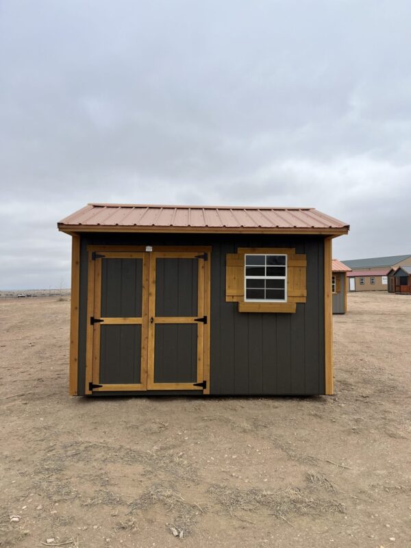 The sun shines through a window of a beach house, illuminating a sandy property with a shed and a building surrounded by a cloud-filled sky.