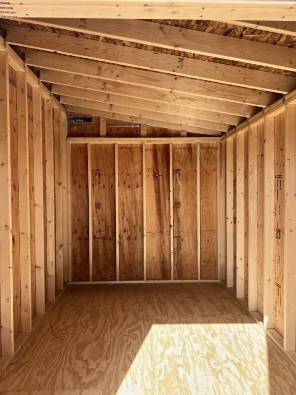 A view of the inside of the 8x12 Urban Style storage shed with a plywood ceiling and floor, wooden beams, and lumber supports.