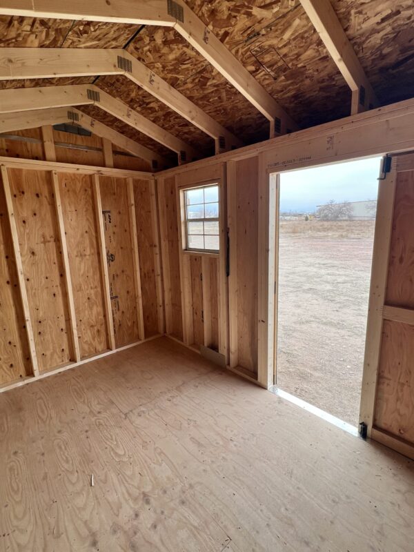 A wooden house is being constructed with hardwood beams, lumber planks, plywood, building insulation, and windows for the ceiling and walls.