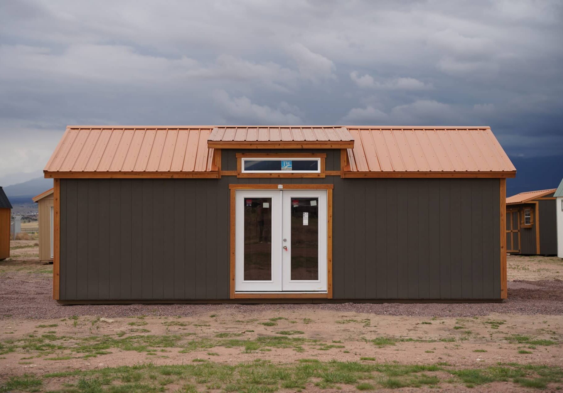Front view of a large Studio Gable 12x28 storage shed with residential-style double doors, grey wood siding, and a metal roof.