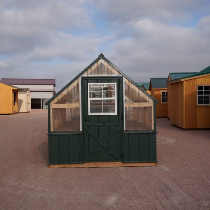 Front view of an 8x12 Green House with wood frame, green metal siding and roof, and plastic covering on the upper walls, highlighting the door in the front.