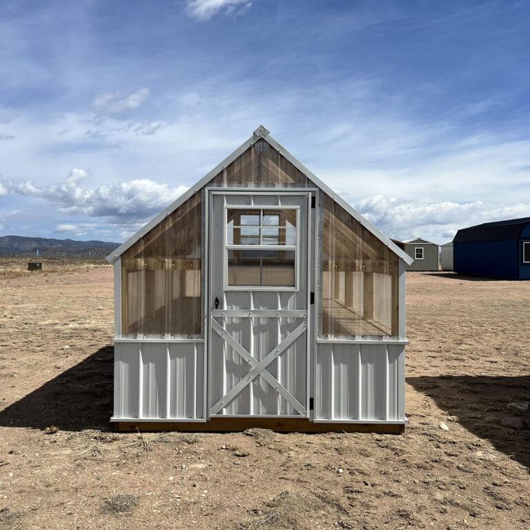 A view of the 8x12 Greenhouse from the front. In the background are other storage sheds and clouds in the sky above the property.